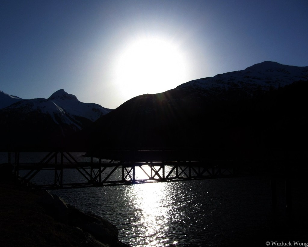 Shadowy bridge over river in setting sun photo for "Fleeting" poem by Winluck Wong, writer based in New Brunswick